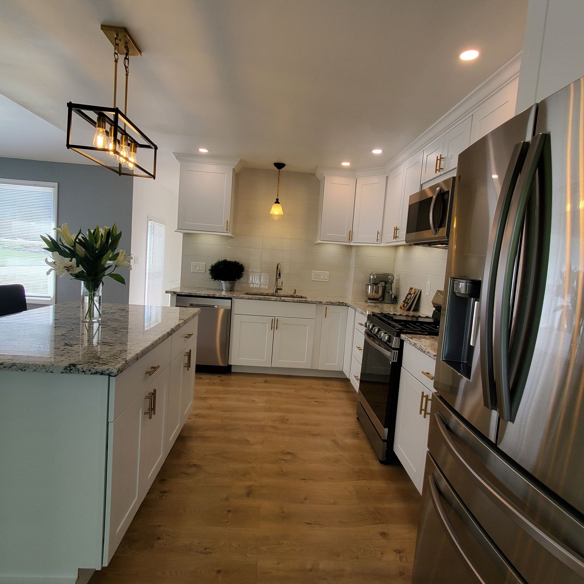 Modern kitchen with white cabinets, stainless steel appliances, granite countertops, and wooden floors.