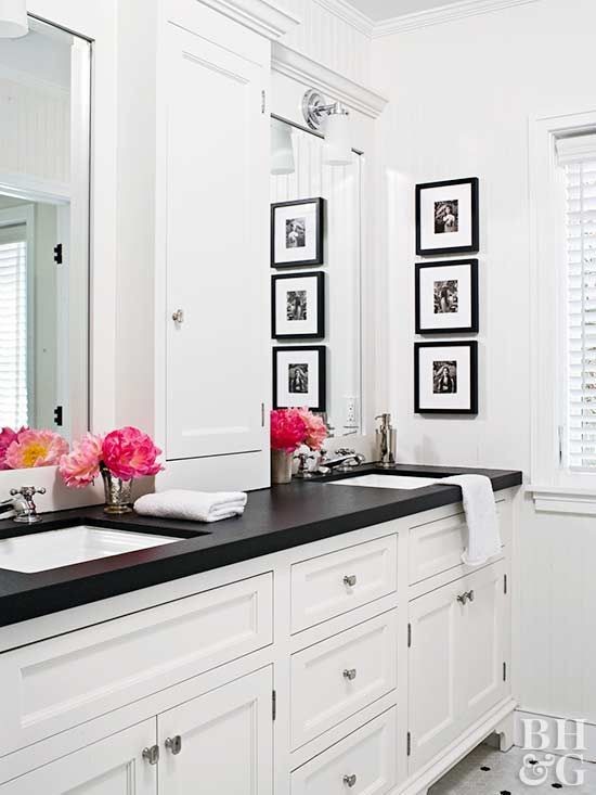 Modern bathroom with white cabinets, black countertop, double sink, framed artwork, and pink flowers.