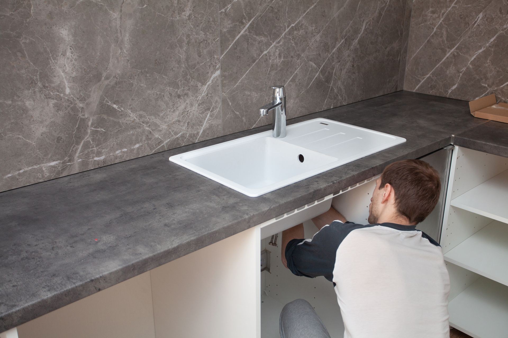 Installation new mixer tap. Unpacking and setting faucet. Plumber fixes a mixer tap. Repairing a kitchen sink at home. Interior in grey and white colors.